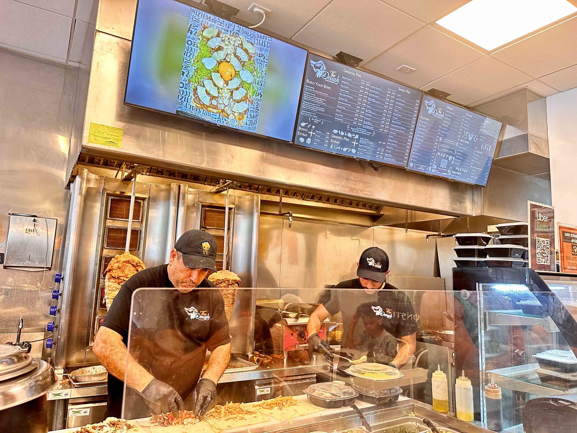 two chefs cooking behind glass with the dough show digital menu above the counter
